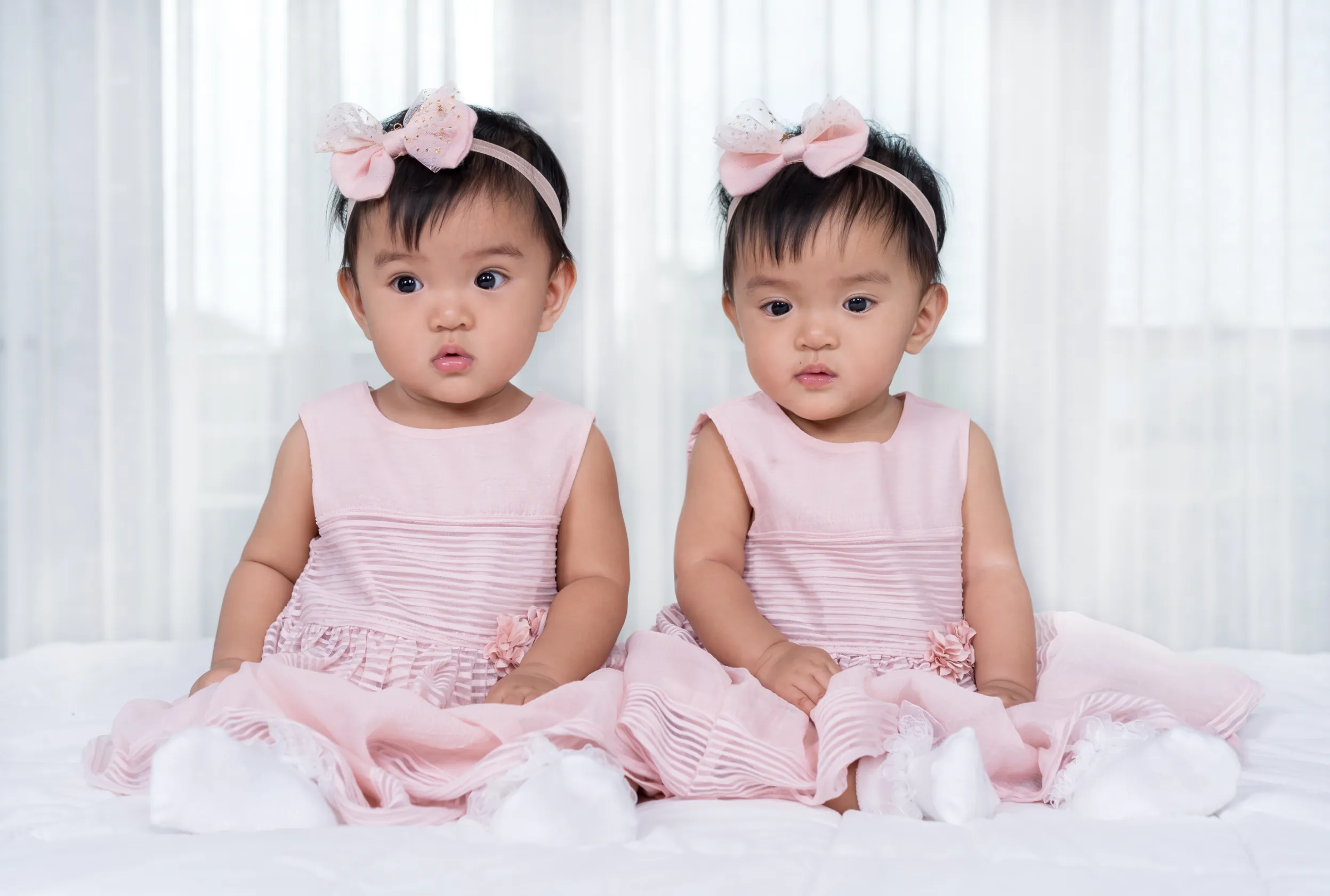 two twin babies in pink dress on a bed